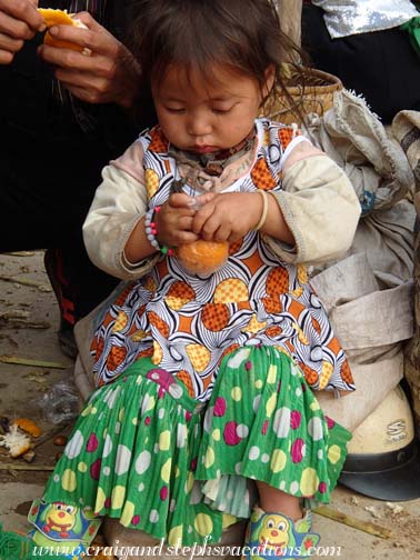 Toddler peels an orange at Dong Van market