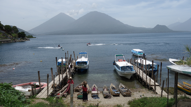 An elderly couple in traditional dress stands in stark contrast to the jet skis in San Antonio Palopo