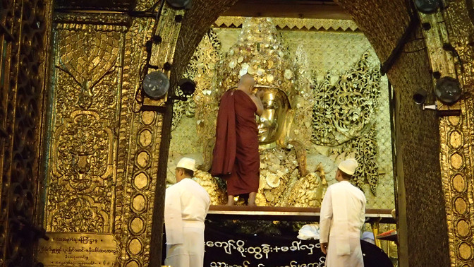 Monk applies resin and gold leaf to Mahamuni Buddha's forehead