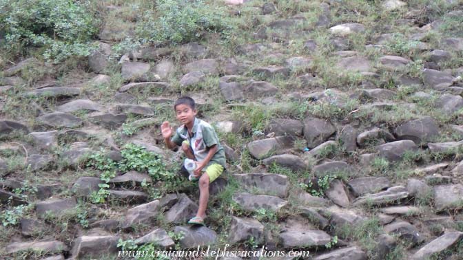 A boy on the shore pours water into holes in the ground to flood out crickets to eat